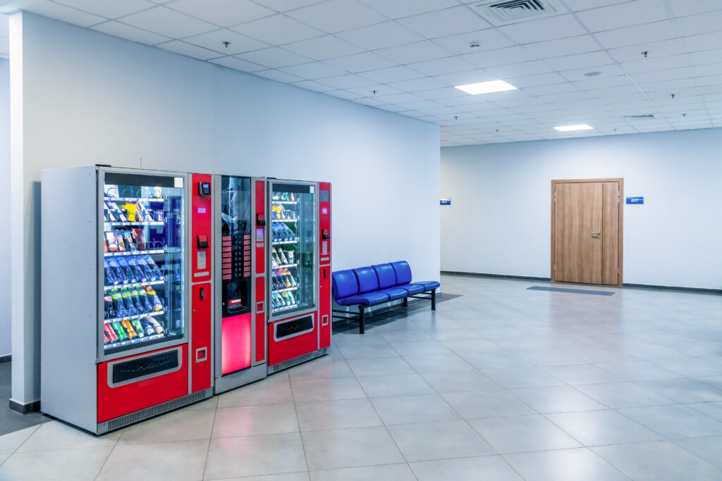 Deux distributeurs automatiques rouges dans un espace public avec sièges d’attente, symbolisant un emplacement idéal pour générer des revenus réguliers.